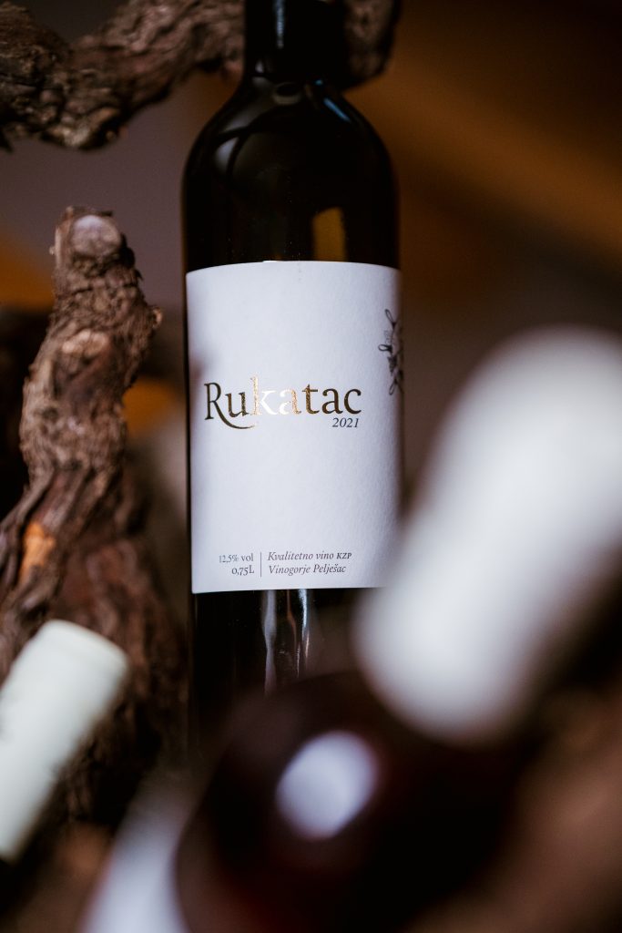 Kvalitetno suho bijelo vino autohtone sorte Rukatac vinarije Škurla na Pelješcu. Boca položena na trs vinove loze u rustikalnom ambijentu.