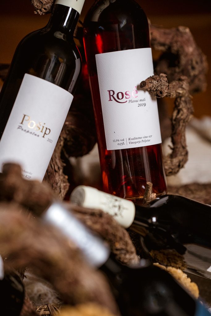 Kvalitetno suho rose vino autohtone sorte plavac mali, vinarije Škurla na Pelješcu. Boca položena na trs vinove loze u rustikalnom ambijentu. S lijeve strane vidi se bijelo vino Pošip